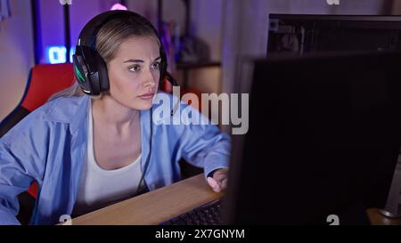 Giovane donna concentrata che gioca a tarda notte in una stanza buia illuminata dalla luce dello schermo Foto Stock