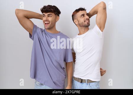 Coppia omosessuale gay in piedi su sfondo bianco sorridente sicuro di toccare i capelli con il gesto della mano in su, in posa attraente e alla moda Foto Stock
