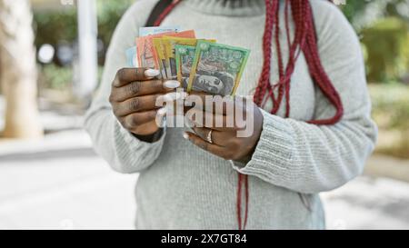 Valuta australiana detenuta da una donna con trecce all'aperto in un parco lussureggiante. Foto Stock