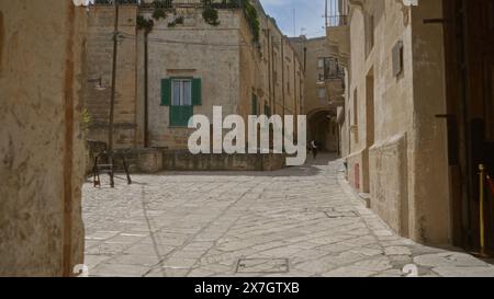 Un uomo cammina attraverso una stretta strada acciottolata nel centro storico di matera, in basilicata, italia, con vecchi edifici in pietra e serrature verdi Foto Stock