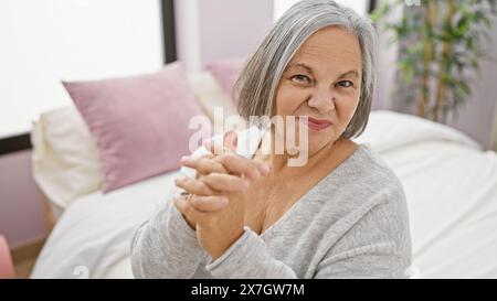 Donna anziana che sorride calorosamente in casa seduto sul letto a casa. Foto Stock