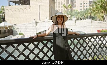 Donna sorridente in un cappello da sole gode dell'acqua panoramica e dell'architettura del suk madinat jumeirah a dubai. Foto Stock