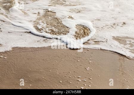 Primo piano dell'acqua di mare spumeggiante su una spiaggia di sabbia Foto Stock