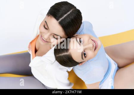 Due graziose ragazze brune in abbigliamento sportivo sedute l'una accanto all'altra su uno sfondo grigio in uno studio. Foto Stock