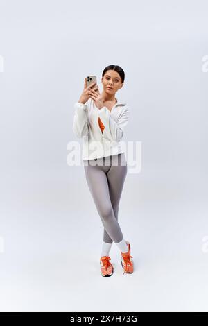 Una ragazza bruna adolescente in abbigliamento sportivo che scatta una foto con il suo cellulare insieme alla sua amica in uno studio. Foto Stock