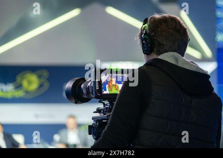 Cameraman che utilizza una videocamera professionale per registrare un evento dal vivo, concentrandosi sull'acquisizione di filmati di alta qualità in uno studio. Foto Stock
