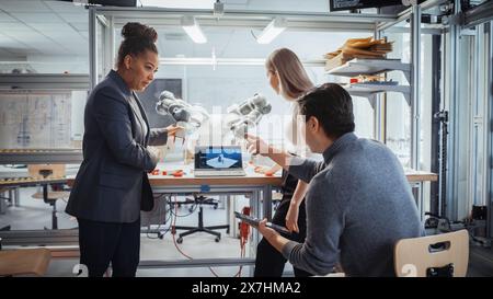 Industry 4,0 High-Tech Factory: Team diversificato di futuri ingegneri robotici che lavorano alla progettazione di bracci robot sotto la supervisione di Black Professor. Tecnologia digitale e concetto di studenti intelligenti. Foto Stock