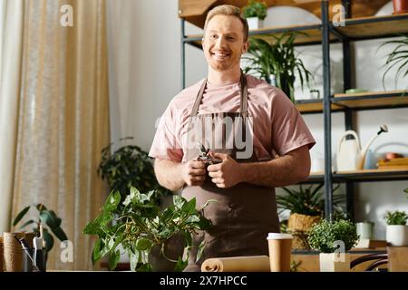 Un bell'uomo si trova nel suo negozio di piante, circondato dal verde e da varie piante in vaso su un tavolo. Foto Stock