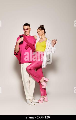 Un uomo e una donna eleganti stanno insieme, la donna con un vestito rosa. La coppia mette in mostra amore e moda in un ambiente studio con sfondo grigio. Foto Stock