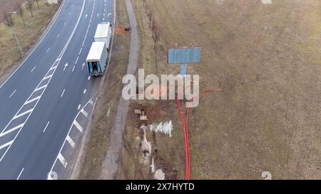 Fotografia con droni di operai edili, macchinari industriali che posano nuove condutture vicino a una strada durante il giorno nuvoloso primaverile Foto Stock