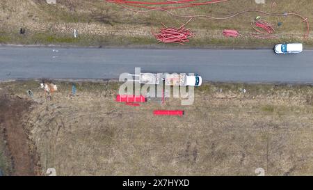 Fotografia con droni di operai edili, macchinari industriali che posano nuove condutture vicino a una strada durante il giorno nuvoloso primaverile Foto Stock