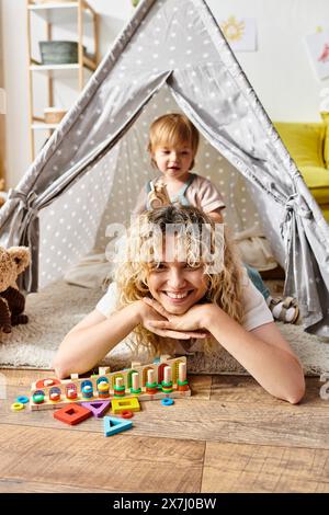 Una madre dai capelli ricci sdraiata sul pavimento con la figlia, esplorando le attività di Montessori a casa. Foto Stock