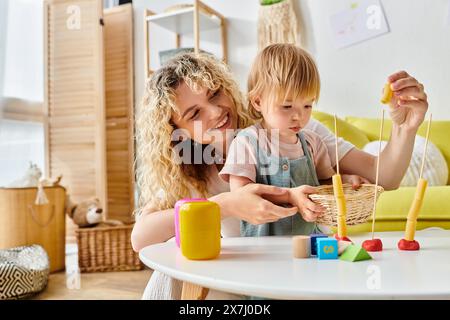 Una madre dai capelli ricci e sua figlia si impegnano a giocare mentre abbracciano il metodo Montessori a casa. Foto Stock