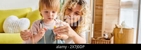 Una madre riccia e la figlia più piccola interagiscono giocosamente con un filo, esplorando il metodo Montessori a casa. Foto Stock