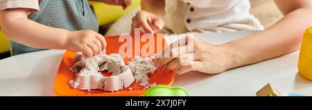 Un bambino con la madre sta scherzosamente sperimentando un piatto usando i principi Montessori. Foto Stock