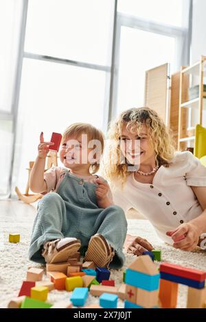 Una madre dai capelli ricci e sua figlia si impegnano in un gioco educativo con blocchi sul pavimento. Foto Stock