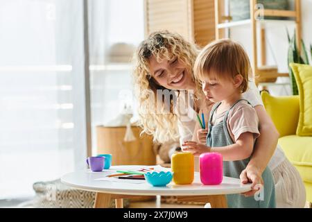 Una madre dai capelli ricci e la figlia del bambino esplorano e imparano giocosamente usando le tazze in un'attività ispirata a Montessori a casa. Foto Stock