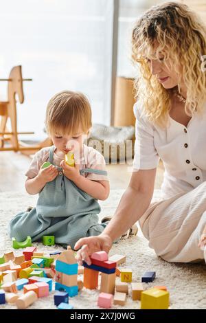 Una madre riccia e la figlia del bambino interagiscono giocosamente sul pavimento usando il metodo di educazione Montessori. Foto Stock