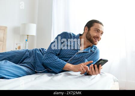 Un uomo che si è impegnato pacificamente con il suo cellulare mentre si è steso su un comodo letto. Foto Stock