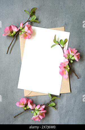 Biglietto d'auguri bianco vuoto con busta marrone e fiori rossi su sfondo grigio. Foto Stock