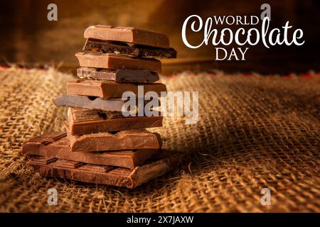 Poster celebrativo della giornata mondiale del cioccolato. Mucchio di pezzi di cioccolato su sfondo rustico Foto Stock