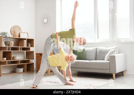 Bella giovane donna sportiva con la sua bambina che pratica yoga a casa Foto Stock