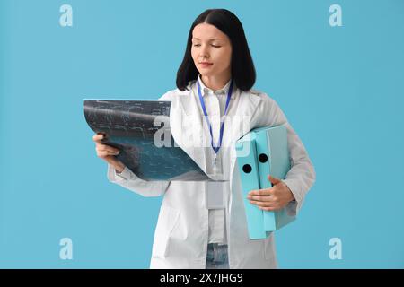 Medico donna con immagine radiografica della colonna vertebrale e cartelle su sfondo blu Foto Stock