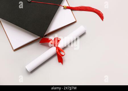 Diploma con nastro rosso, libro aperto e cappello graduato su sfondo bianco Foto Stock