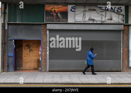 Una donna che passa davanti a un negozio chiuso, High Street, Strood, Kent, Regno Unito. 23 aprile 2024 Foto Stock