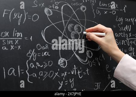 Insegnante che scrive formule fisiche con gesso su lavagna nera, primo piano Foto Stock