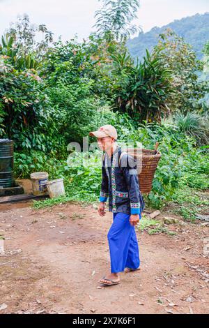 Un giovane che porta un cesto di vimini vestito con un tipico abbigliamento paj ntaub o un panno floreale Hmong, Chiang Khong, provincia di Chiang Rai, Thailandia settentrionale Foto Stock