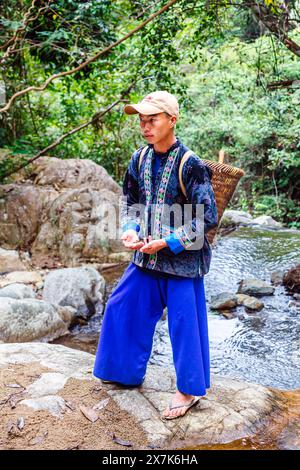 Un giovane che porta un cesto di vimini vestito con un tipico abbigliamento paj ntaub o un panno floreale Hmong, Chiang Khong, provincia di Chiang Rai, Thailandia settentrionale Foto Stock