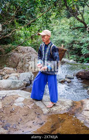 Un giovane che porta un cesto di vimini vestito con un tipico abbigliamento paj ntaub o un panno floreale Hmong, Chiang Khong, provincia di Chiang Rai, Thailandia settentrionale Foto Stock