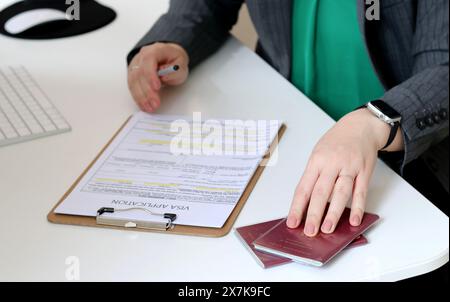 Vista dall'alto di una donna che compila i documenti per la richiesta di visto con un passaporto tedesco su un tavolo dell'ufficio Foto Stock