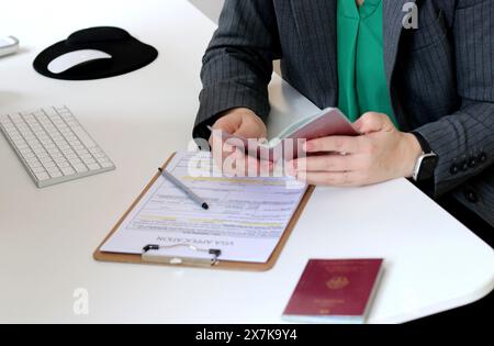 Vista dall'alto di una donna che compila i documenti per la richiesta di visto con un passaporto tedesco su un tavolo dell'ufficio Foto Stock