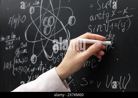 Insegnante che scrive formule matematiche con gesso sulla lavagna, primo piano Foto Stock