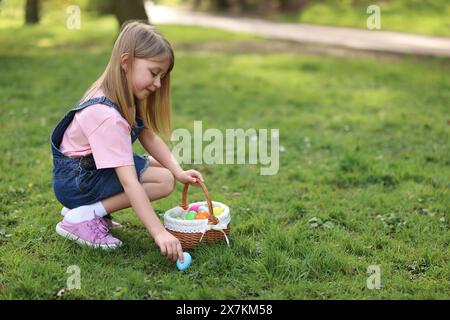 Festa di Pasqua. Bambina carina con orecchie da coniglio che caccia uova all'aperto, spazio per il testo Foto Stock