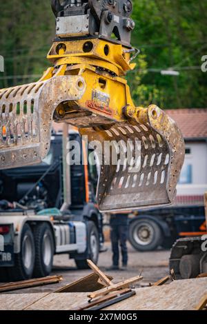 Braccio giallo per escavatore con benna a polipo in cantiere, trucioli di legno e camion sullo sfondo, demolizione, Saarbruecken, Germania Foto Stock