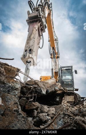 Un escavatore in un cantiere che lavora su un mucchio di macerie, grandi pezzi di metallo accanto ad esso, cielo nuvoloso grigio, demolizione, Saarbruecken, Germania Foto Stock