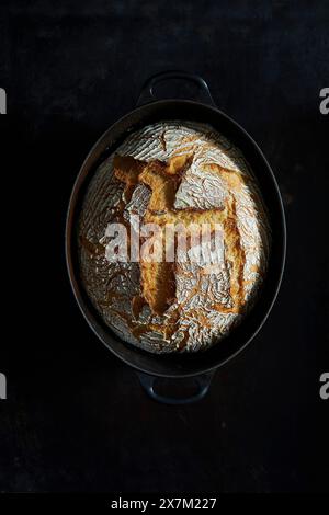 Pane di frumento appena sfornato in una pentola di ghisa su sfondo scuro Foto Stock