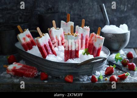 Lo yogurt alla fragola fatto in casa si prepara su ghiaccio tritato in una ciotola di metallo su fondo grigio metallico Foto Stock