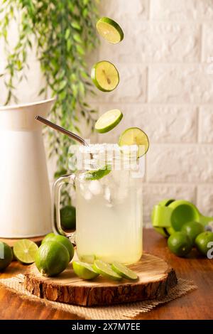 Fette di limoni freschi che cadono sul bicchiere con limonata fatta in casa, bicchiere con paglia metallica e decorato con fette di limone. Foto Stock