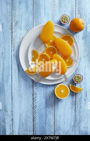 Papaveri di frutta della passione arancia su fette di arancia appena tagliate su un piatto bianco, su sfondo blu Foto Stock