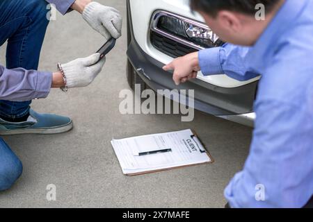 Due persone ispezionano i danni su un veicolo. Il proprietario dell'auto indica un'ammaccatura sul paraurti dell'auto. Uno staff assicurativo che scatta foto con lo smartphone Foto Stock