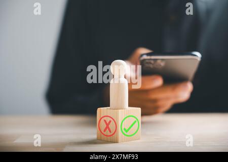 L'uomo d'affari su smartphone controlla i simboli giusti o sbagliati su blocchi di legno pensando sì o no Foto Stock