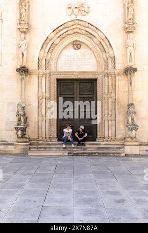 I turisti seduti all'ingresso laterale della spettacolare Cattedrale di San Giacomo nella parte storica della città vecchia di Sibenico, Dalmazia, Croazia Foto Stock