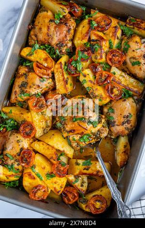 Cosce di pollo al forno, patate e pomodori ciliegini guarniti con prezzemolo in una teglia da forno fotografata dall'alto. Foto Stock