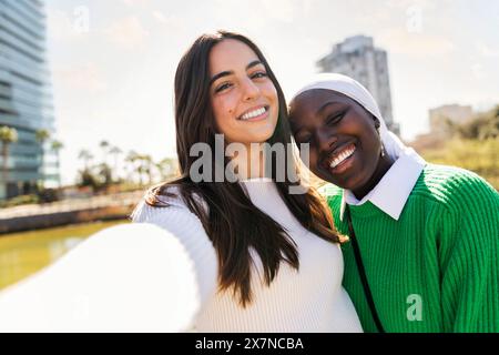 foto selfie di due giovani amiche sorridenti felici e spensierati in un parco cittadino, concetto di diversità e stile di vita moderno Foto Stock