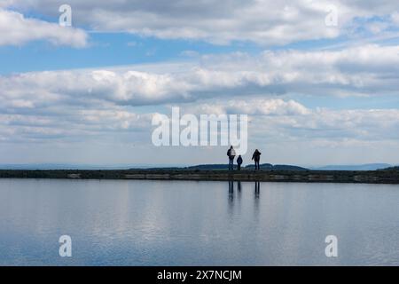 Tre persone sono posizionate su un molo, guardando su un tratto d'acqua Foto Stock