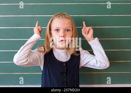 una piccola bellezza di uno studente di prima elementare in una scuola vicino al consiglio risolve il problema. emozioni delle studentesse Foto Stock